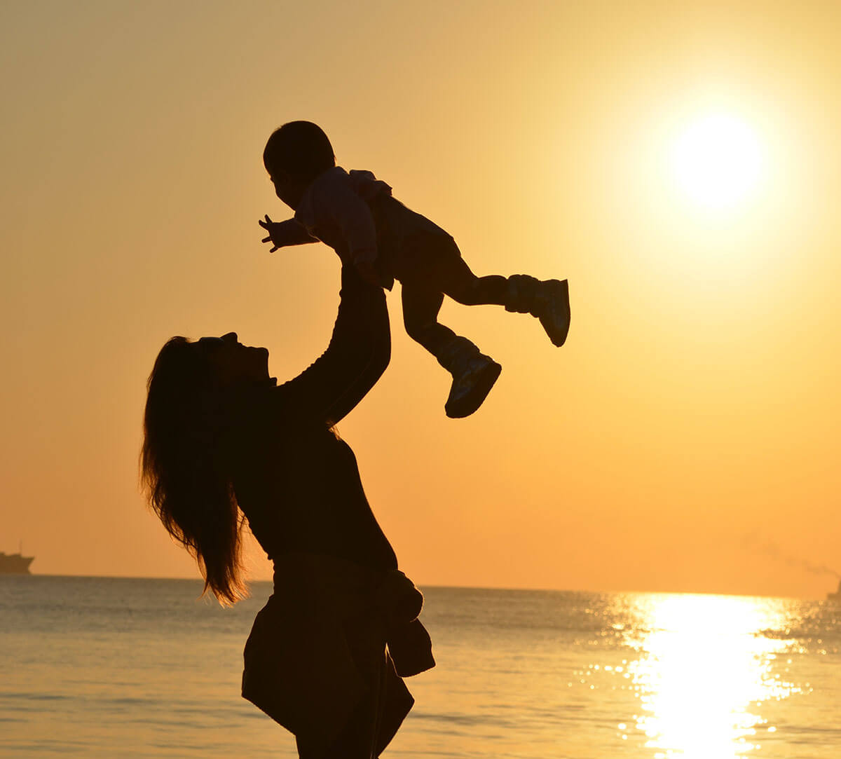 una donna che tiene in alto il bambino al tramonto